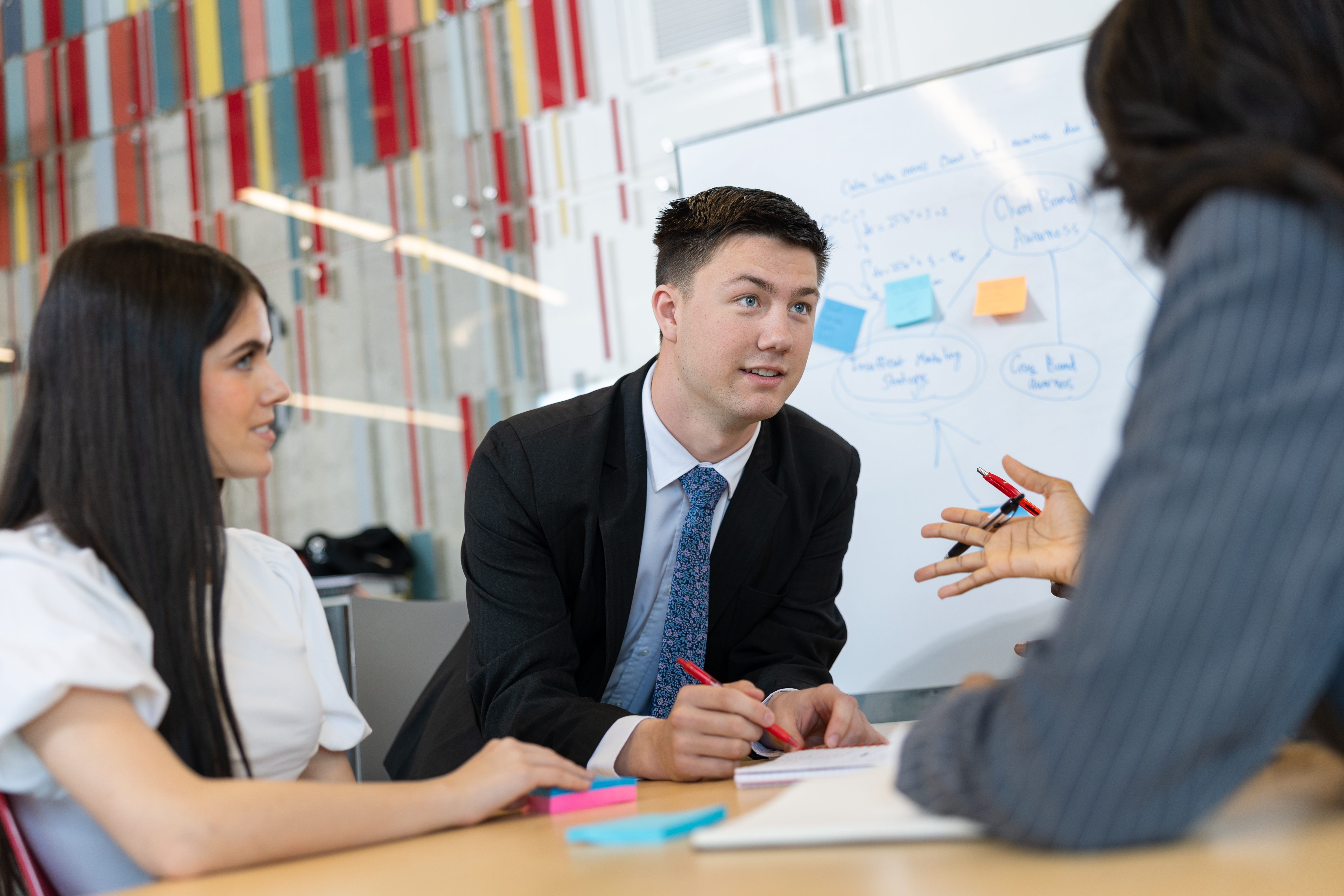 Professionals discussing ideas at a meeting table with a whiteboard in the background.