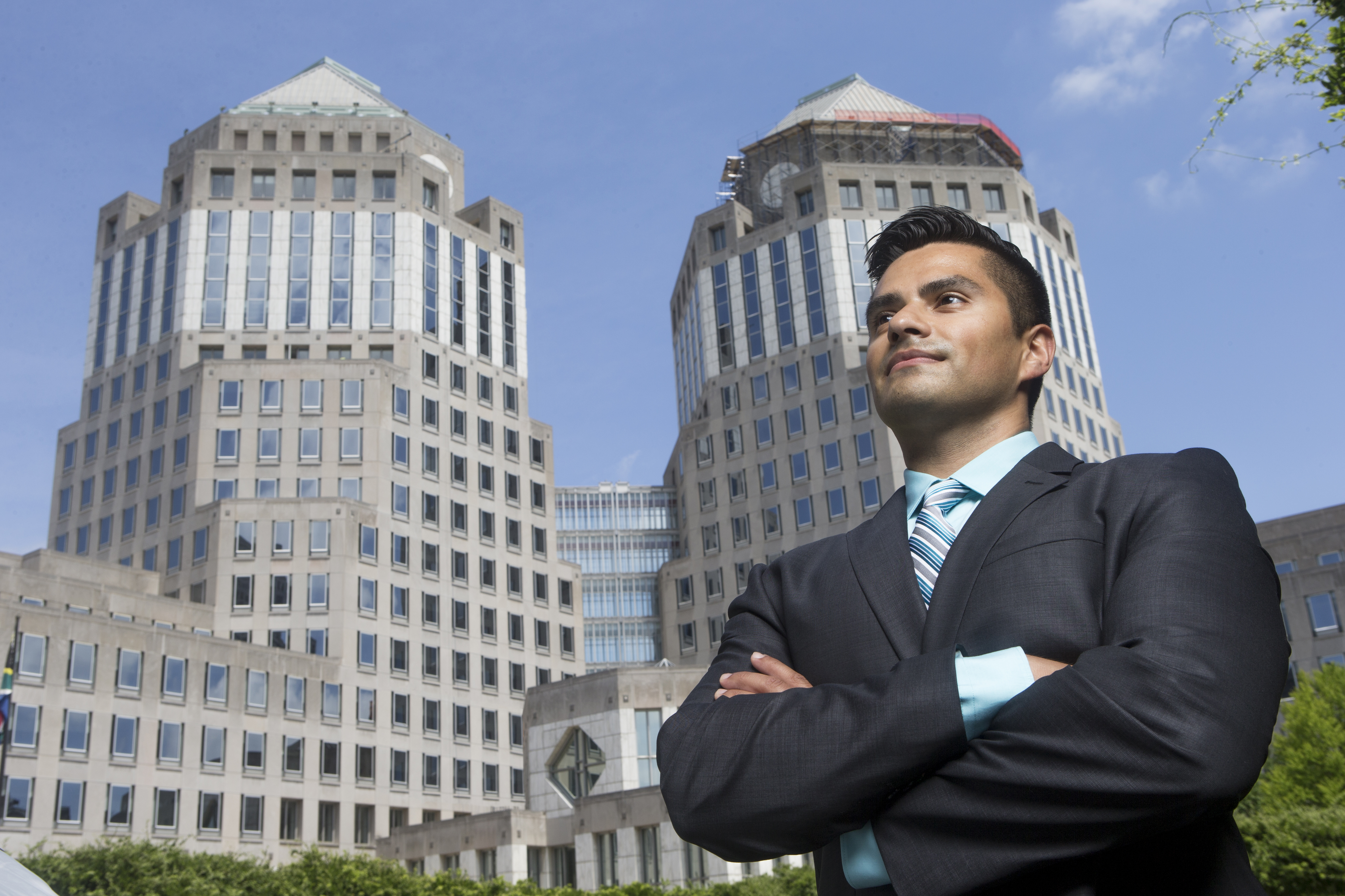 Business professional standing confidently with arms crossed outside modern office buildings