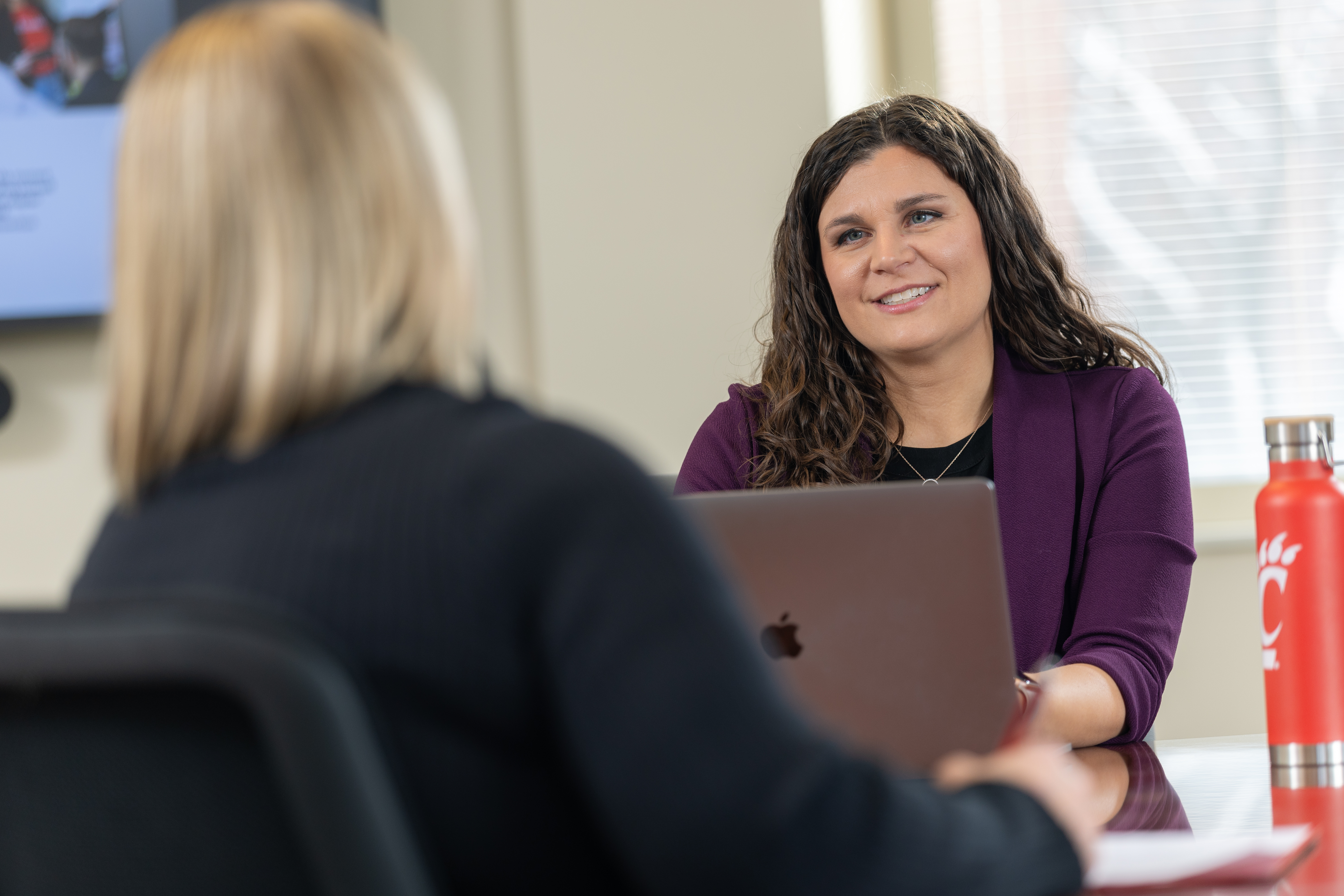 Two people having a conversation across a table, one using a laptop.