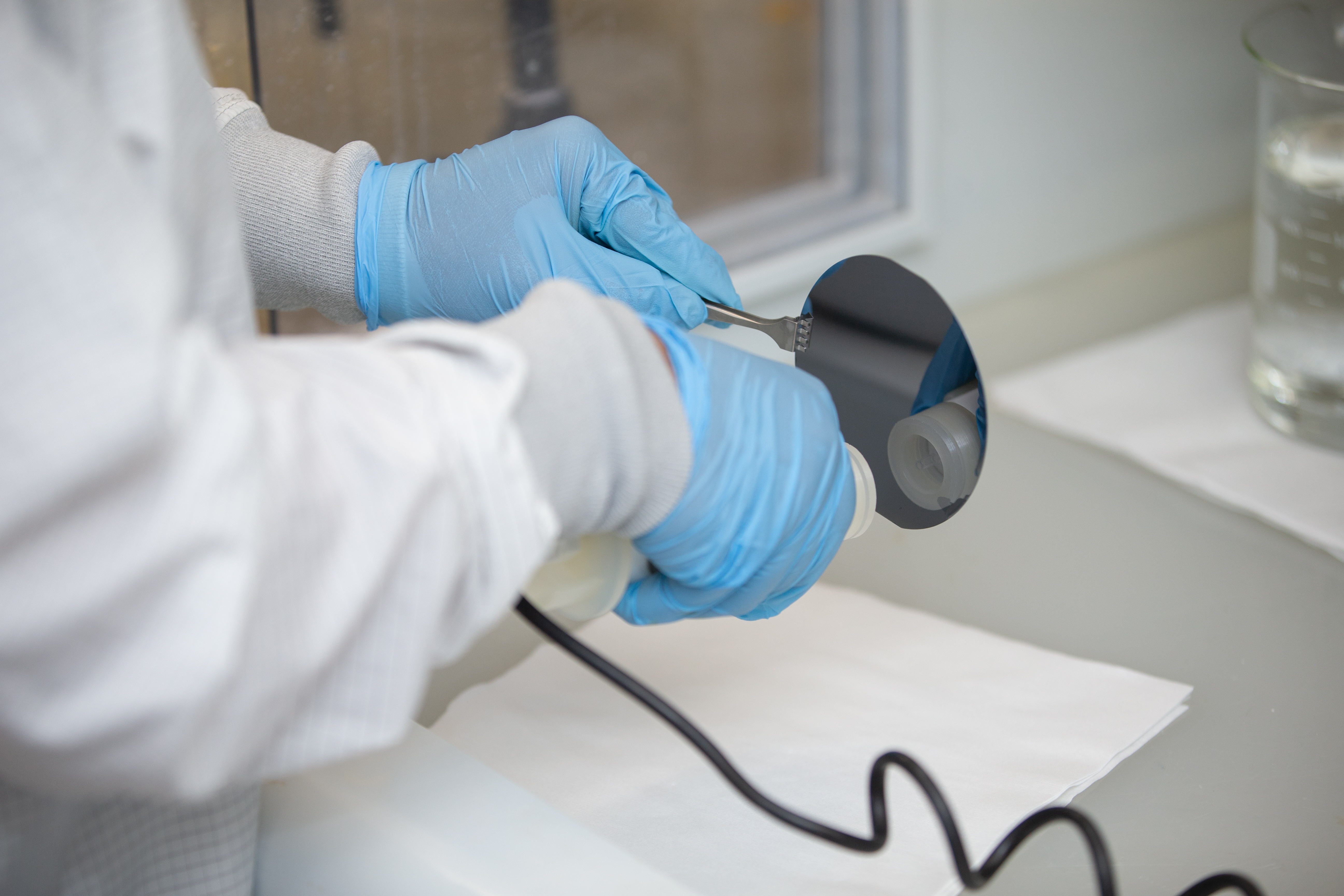 Technician handling a semiconductor wafer with precision tools in a lab setting