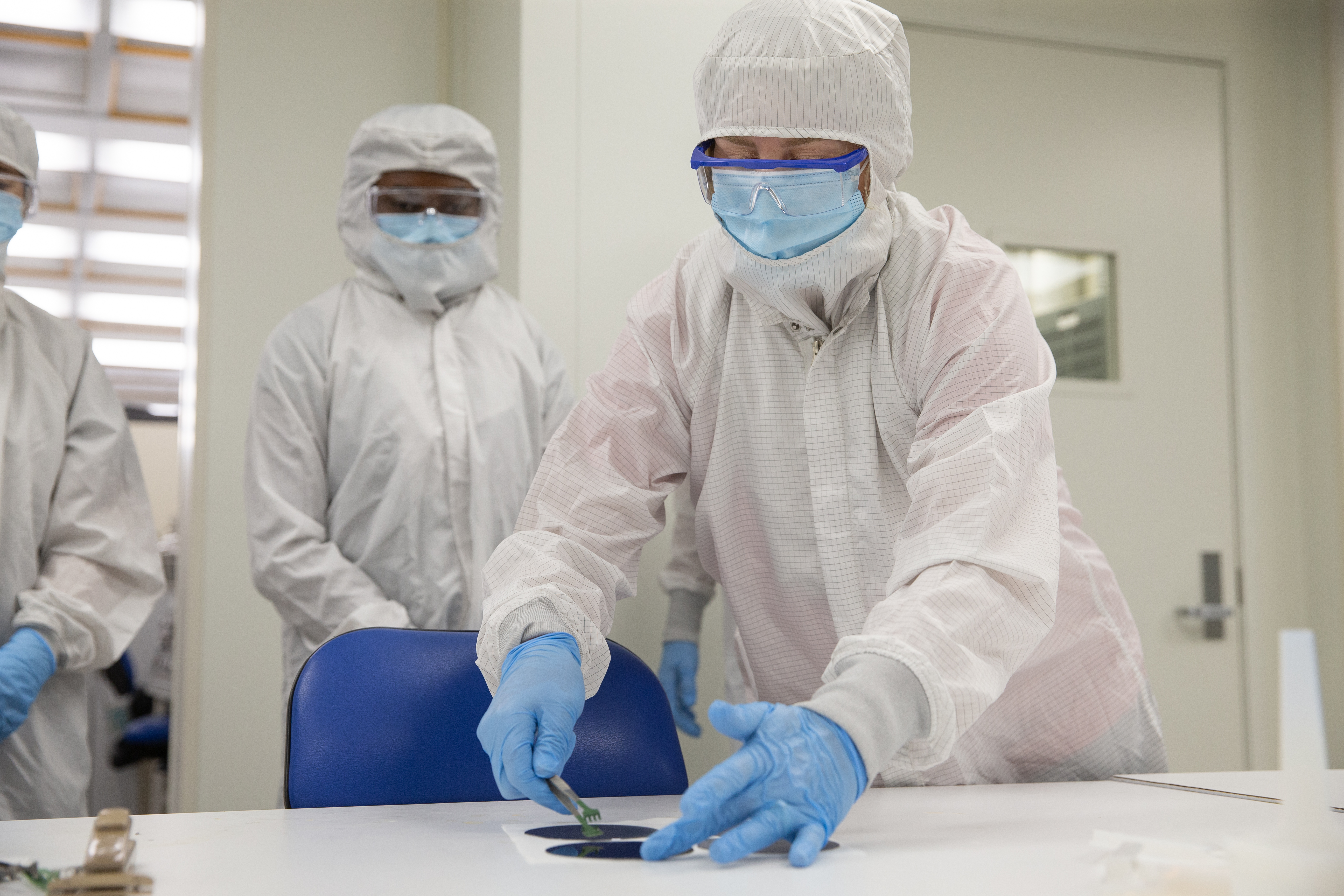 Technician in cleanroom attire handling a semiconductor wafer with precision tools