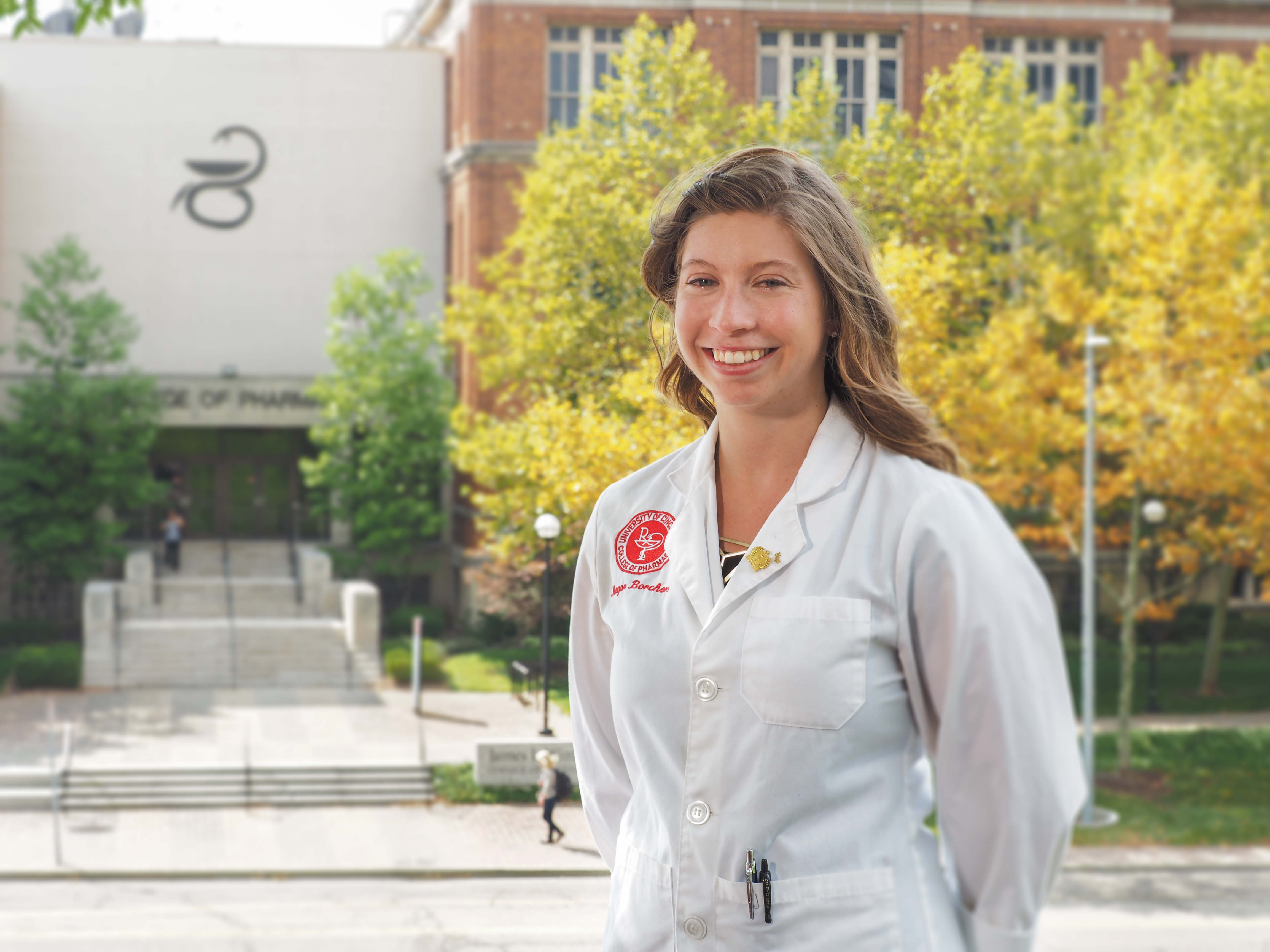 Person in a white lab coat smiling outdoors