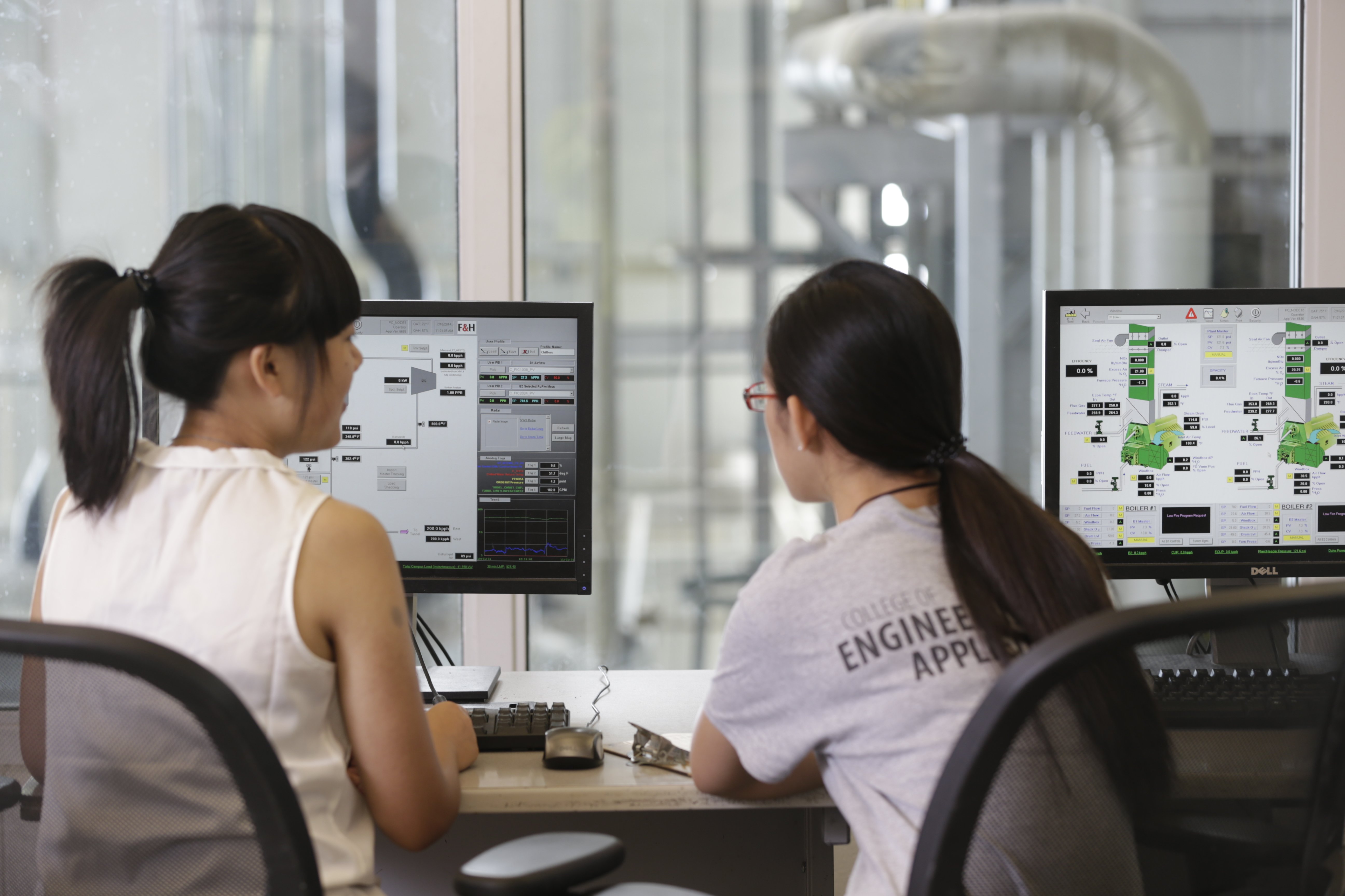 Two individuals collaborating at computers analyzing data on dual monitors