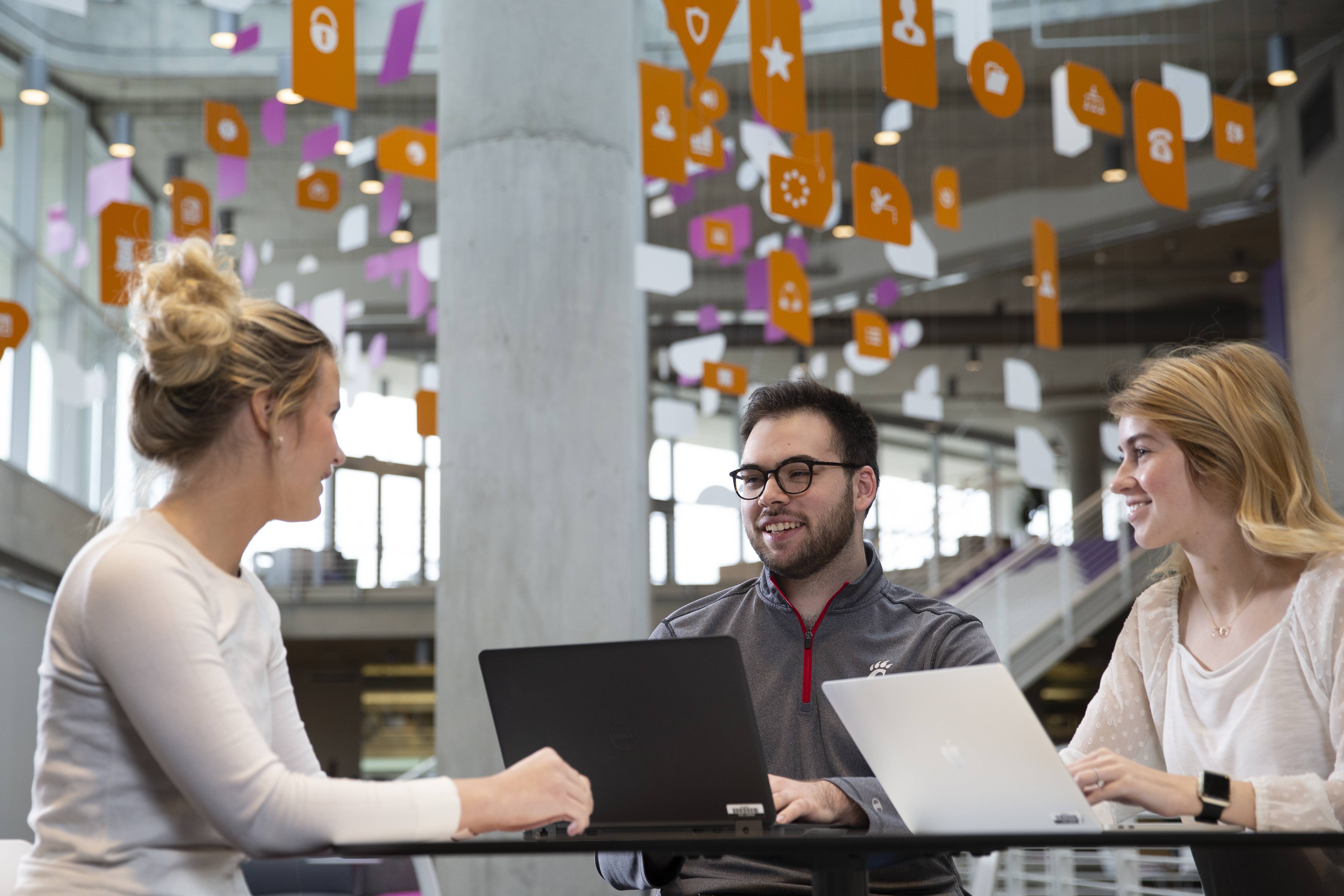 Three people collaborating with laptops in a modern building