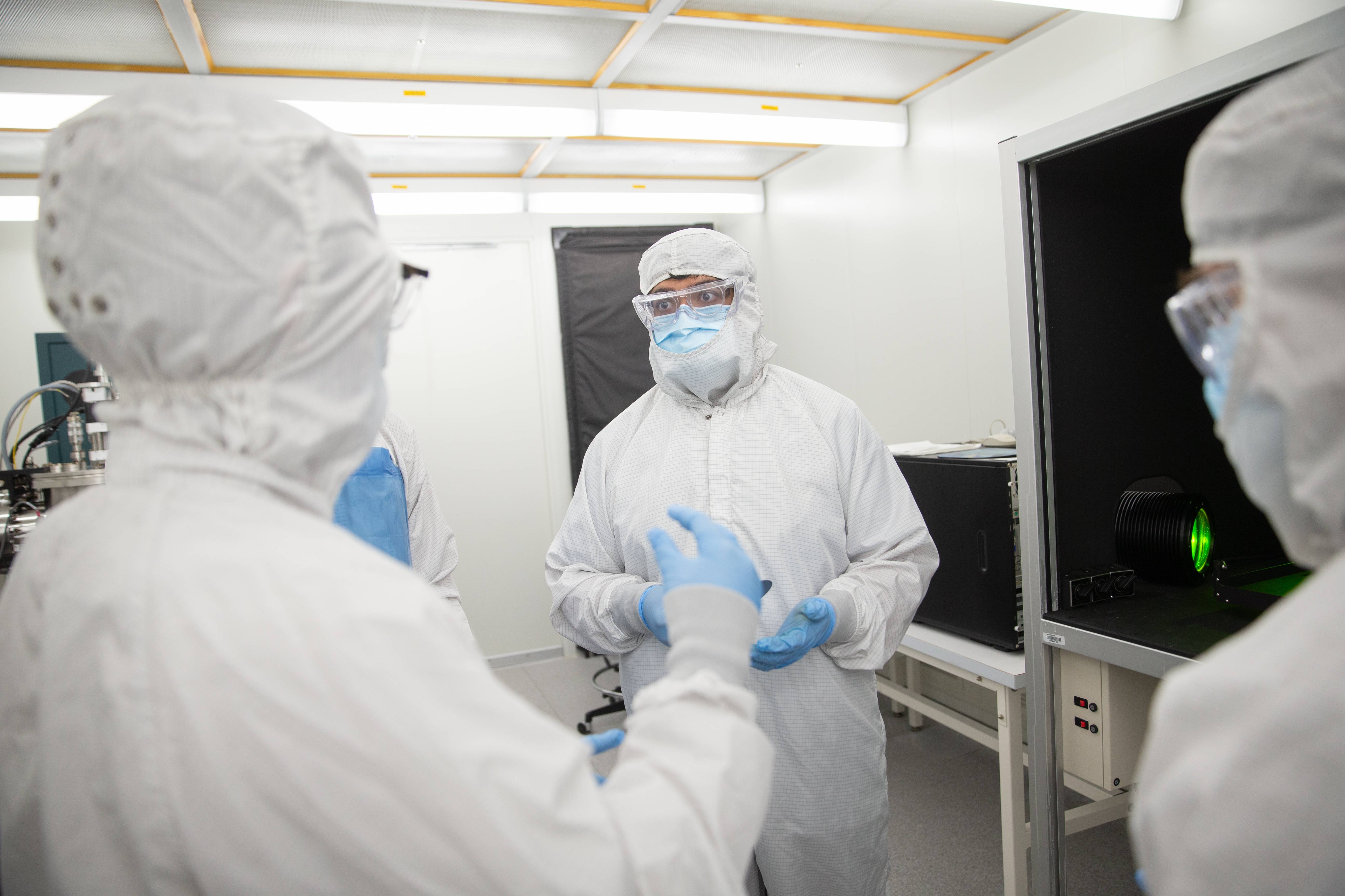 Cleanroom technicians in protective gear discussing semiconductor processing procedures in a lab environment