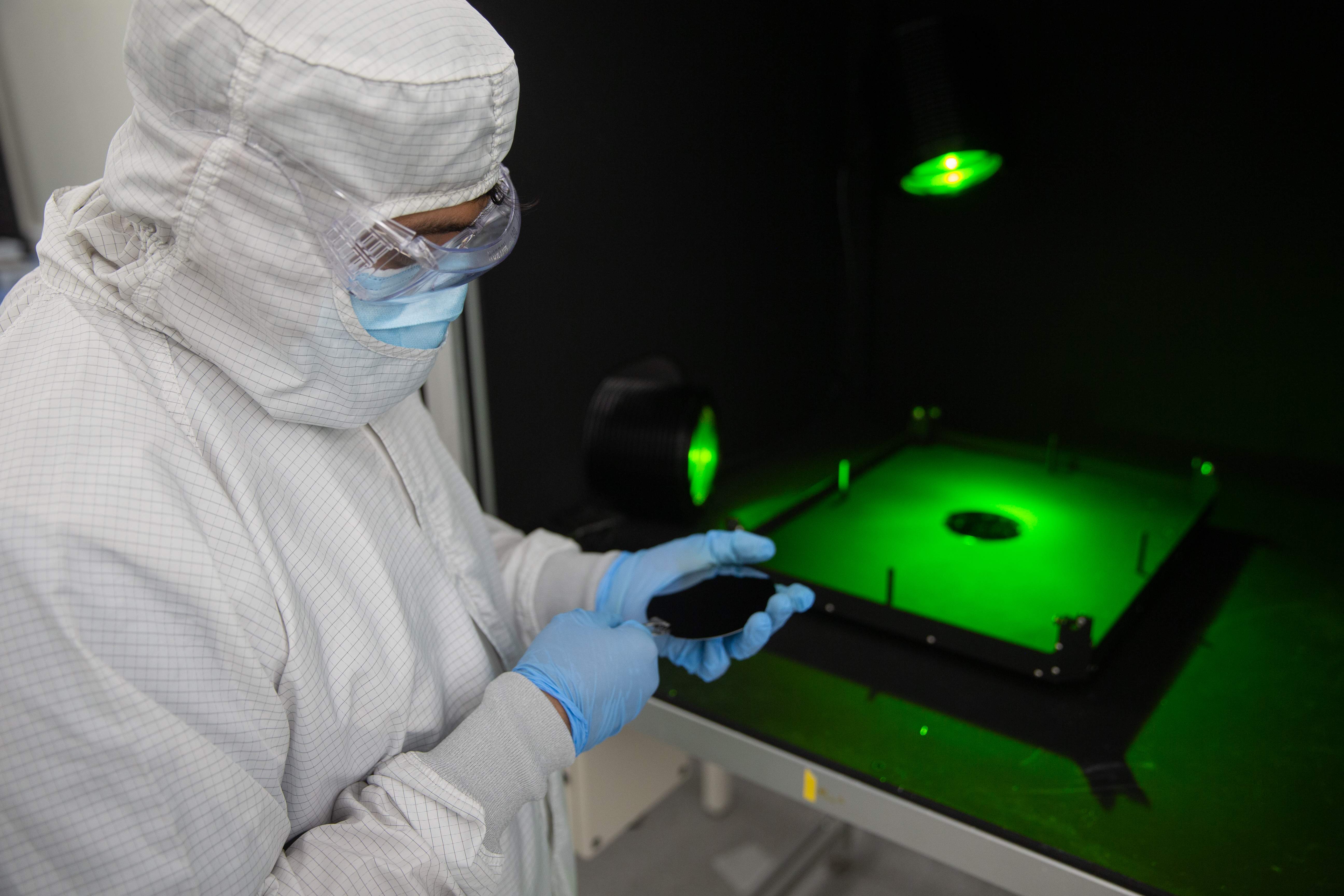 Cleanroom technician using precision tools to handle a semiconductor wafer under green inspection lighting