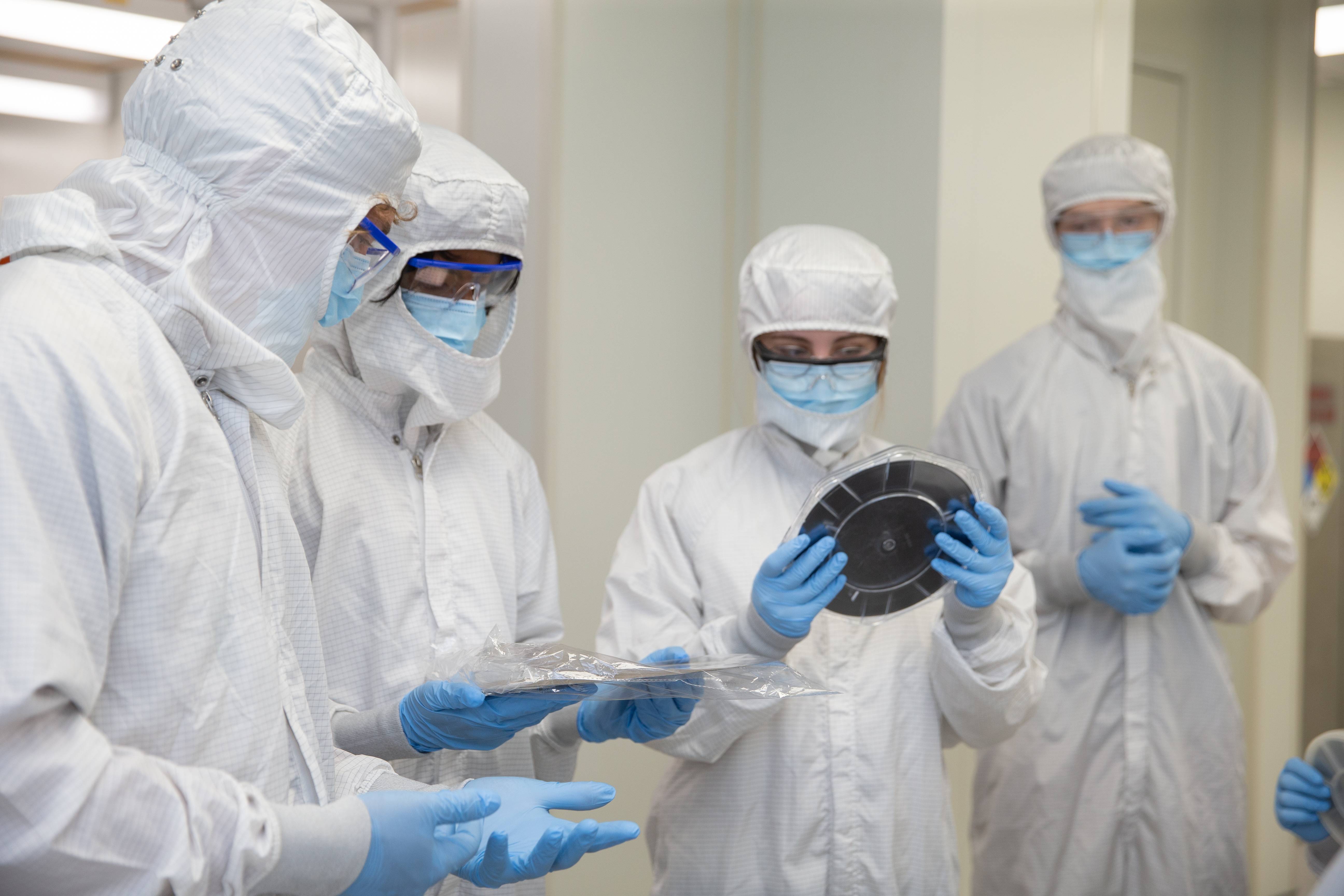 Cleanroom technicians in protective suits examining semiconductor wafers and materials in a lab setting