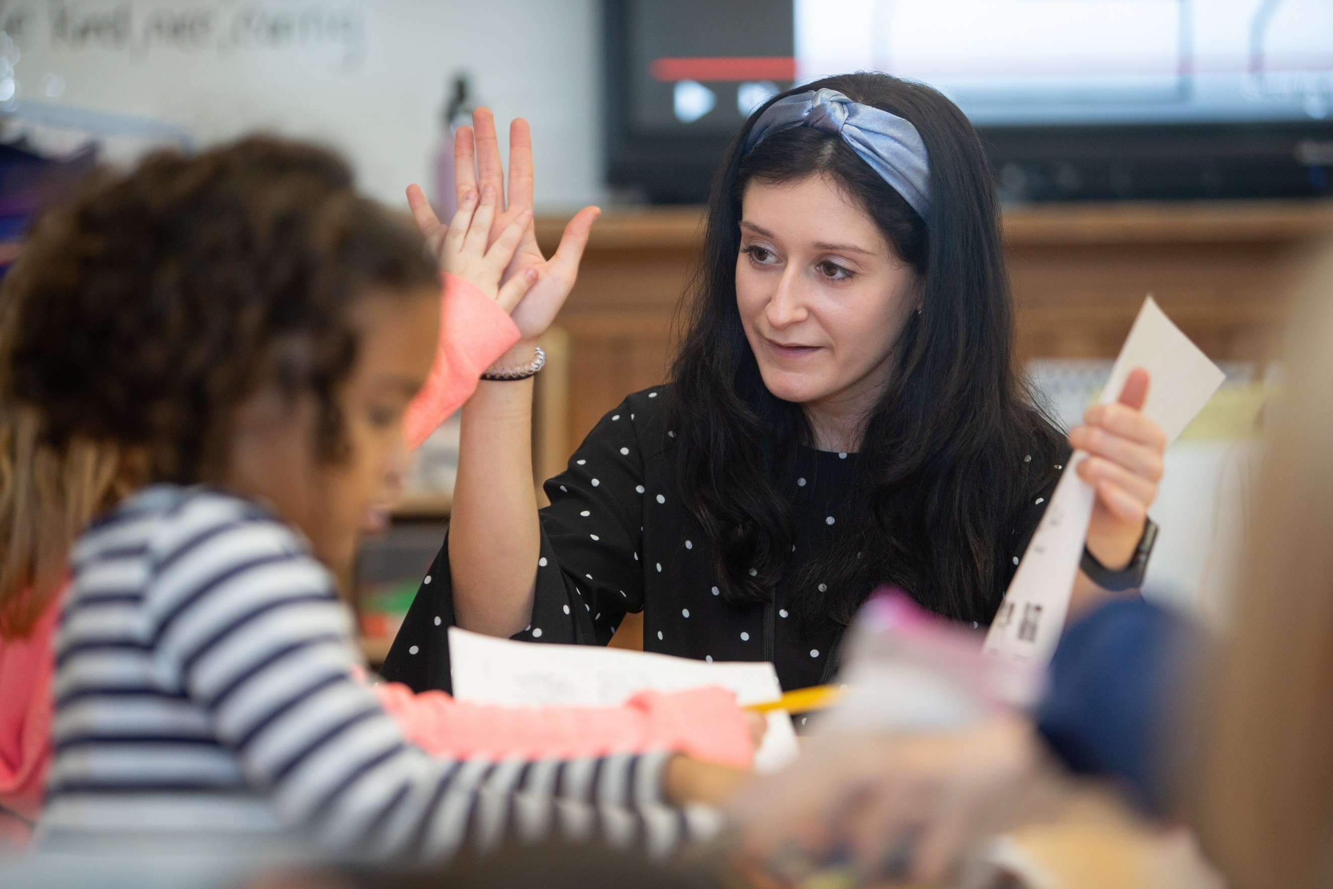 Teacher raising her hand while assisting students at a table