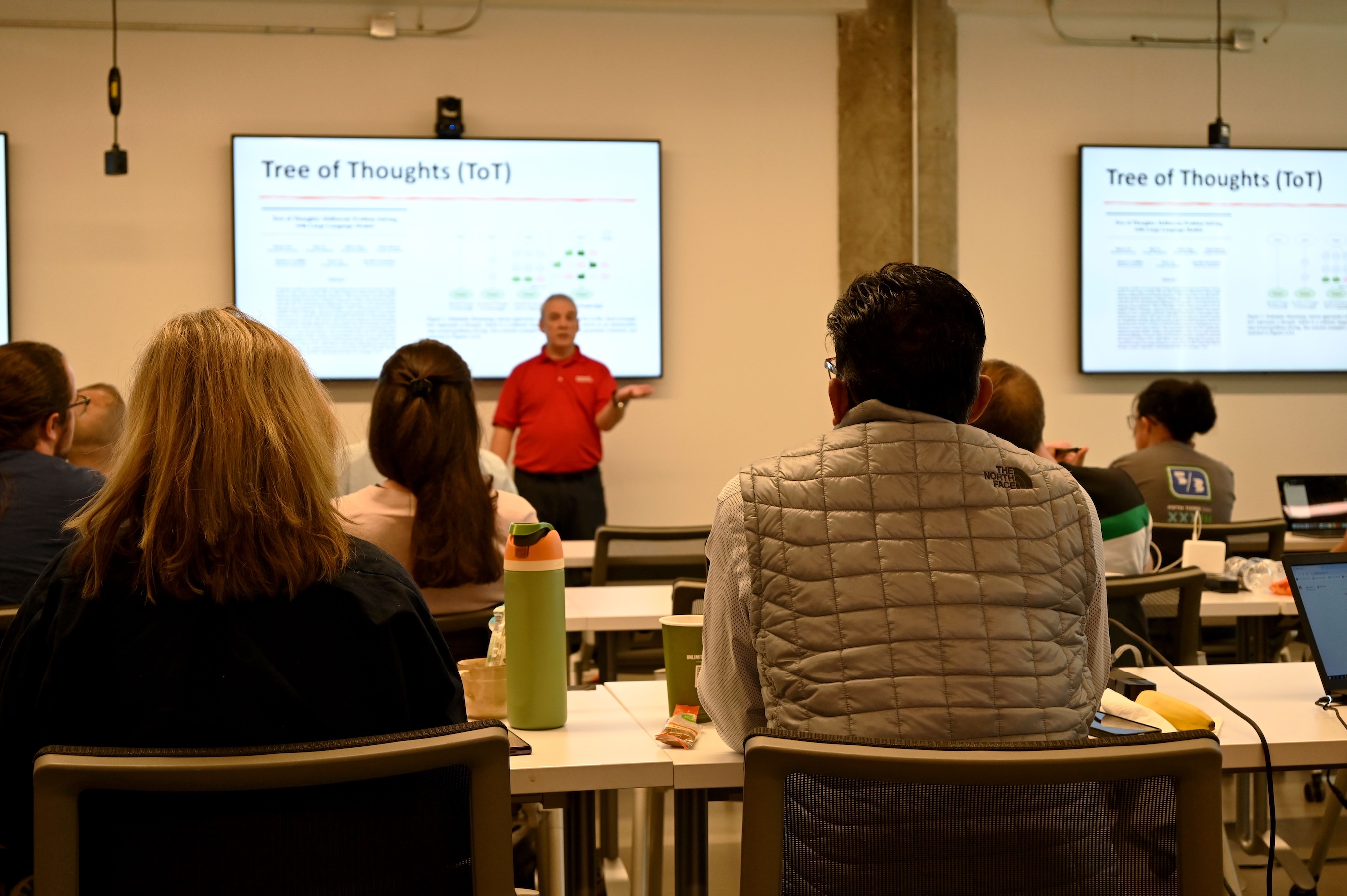 An instructor presents to learners seated at tables during a classroom training session